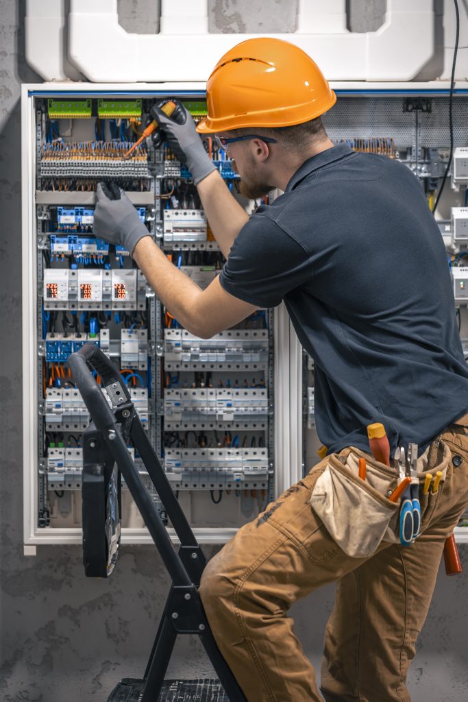 Male electrician working in a switchboard with fuses. Installation and connection of electrical equipment. Professional with tools in hand.